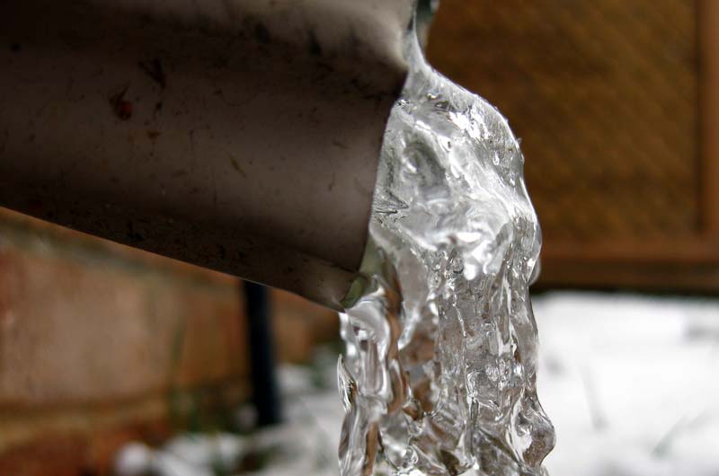 Water flowing from a downspout, illustrating plumbing maintenance and potential winter plumbing issues.