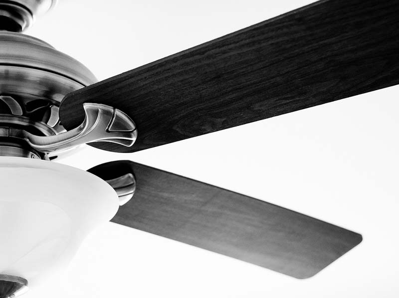 Ceiling fan with wooden blades and a white light fixture, illustrating energy-efficient cooling solutions for home comfort.