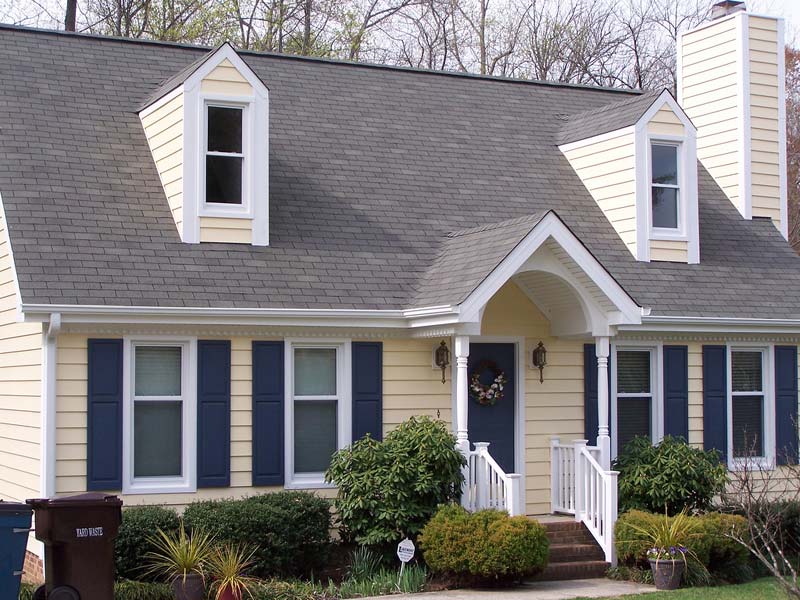 Charming yellow house with blue shutters and a welcoming porch, surrounded by lush greenery, illustrating home exterior improvements and curb appeal tips.