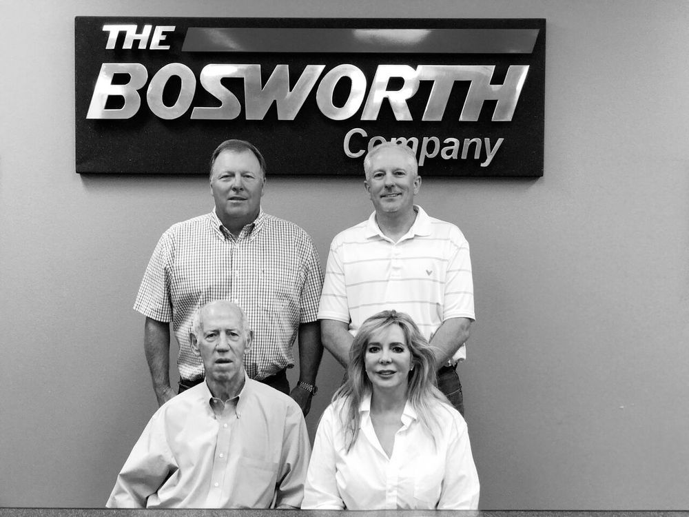 Team members of The Bosworth Company posing in front of company logo, highlighting leadership and commitment to HVAC and plumbing services in Kerrville, TX.