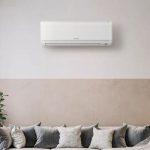 Ductless mini-split air conditioning unit mounted on a wall above a modern sofa with decorative pillows, representing energy-efficient heating and cooling solutions for individual rooms.