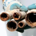 Corroded plumbing pipes held by gloved hands, illustrating the importance of repiping services for homeowners in Kerrville, TX.