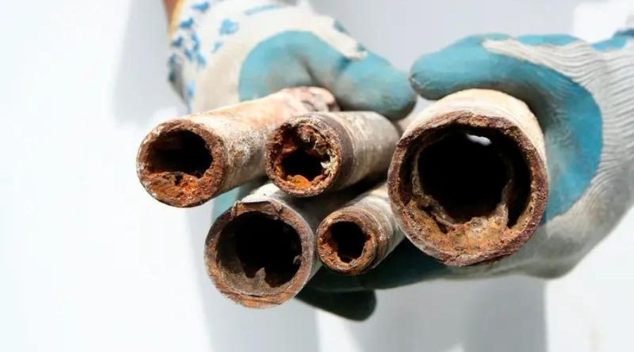 Gloved hands inspect rusty metal pipes, emphasizing plumbing issues for Kerrville's water heater services.