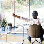 Man sitting in a modern chair with arms outstretched, enjoying fresh air and natural light in a bright, airy office space, symbolizing the benefits of improved indoor air quality from air filtration systems.