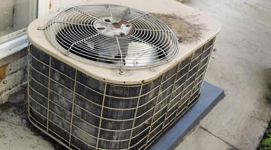Old air conditioning unit with dust and rust, placed on concrete slab by The Bosworth Company Kerrville HVAC services.